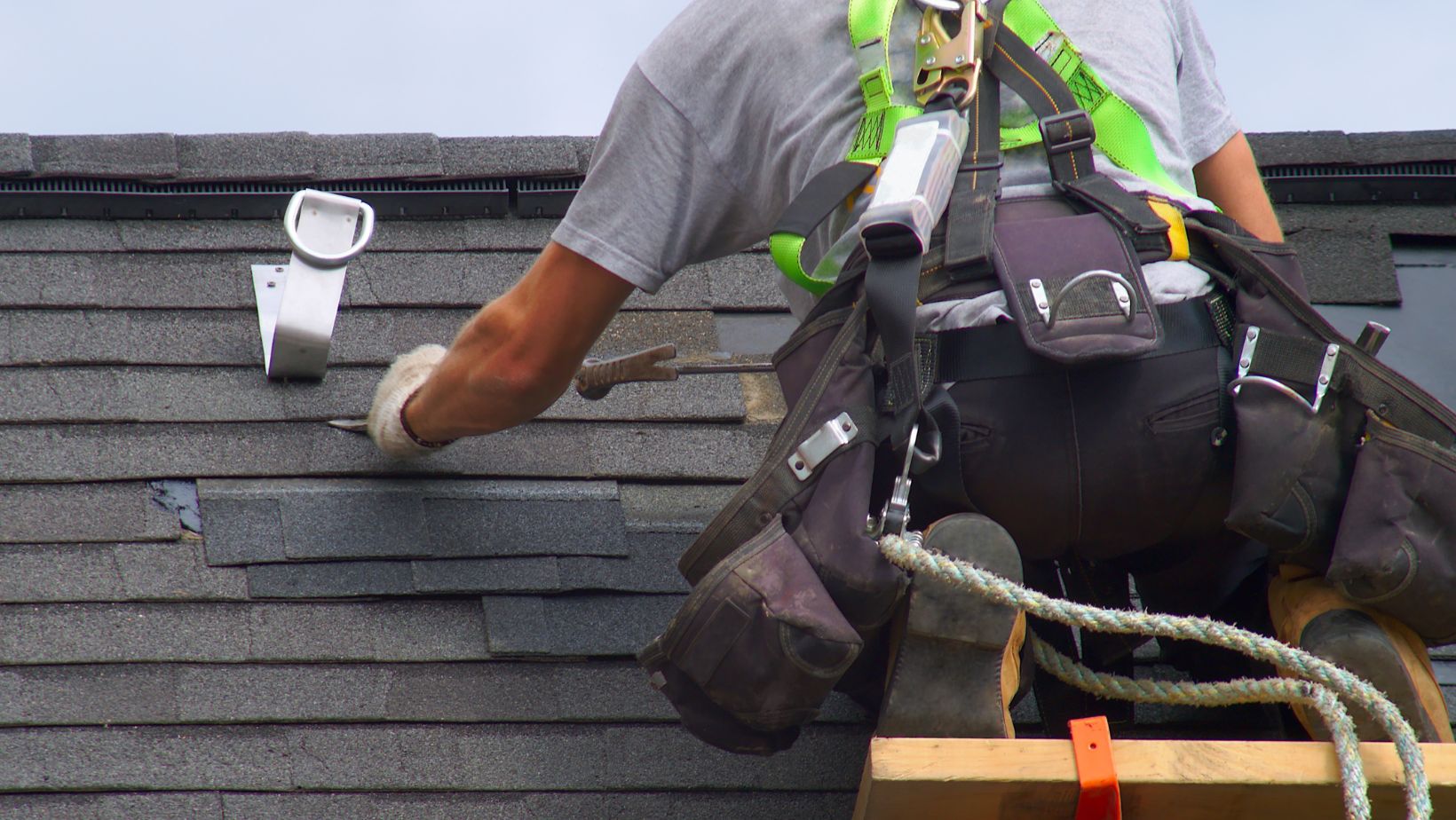 Roofing contractor wearing a safety harness and tool belt installing asphalt shingles on a residential roof. Proper installation ensures durability, weather resistance, and long-lasting protection. Empire Contractors specializes in expert roof installation and repair services.