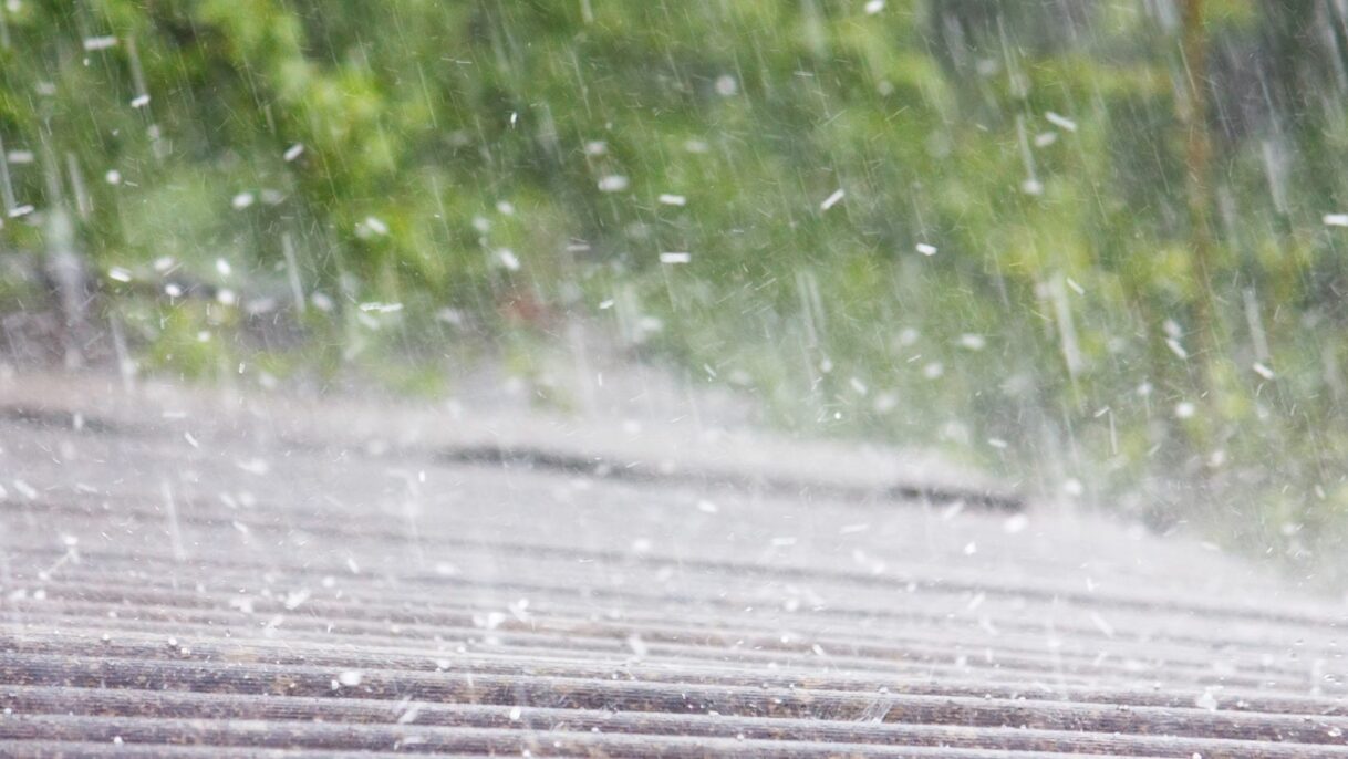 A residential roof being pelted by hail during a storm, highlighting potential damage risks such as dented shingles and leaks. Empire Contractors LLC provides expert hail damage roof repair and replacement services in Cincinnati, OH, and surrounding areas.