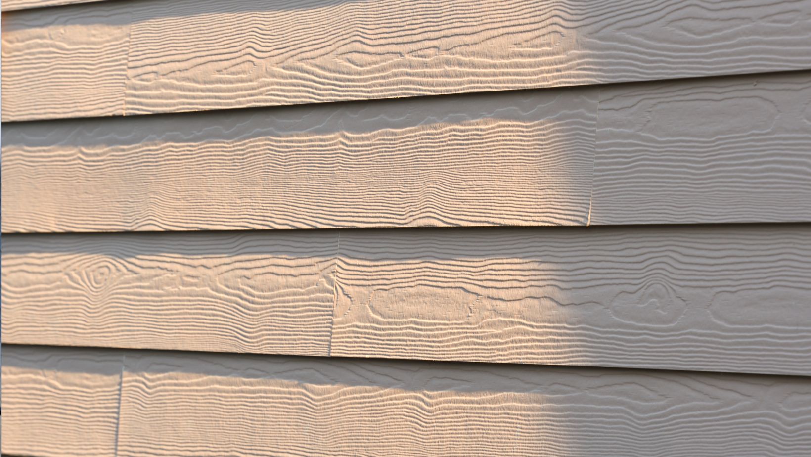 Close-up of beige fiber cement siding with a wood grain texture, illuminated by sunlight. Durable and weather-resistant, fiber cement siding is a long-lasting option for home exteriors. Empire Contractors specializes in professional siding installation for enhanced curb appeal and protection.