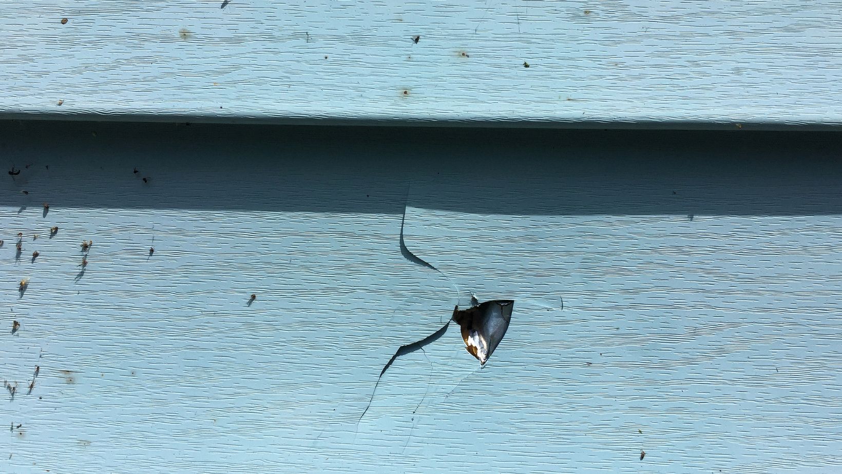 Close-up of damaged blue vinyl siding with a large crack and hole, exposing the material underneath. Signs of wear, impact damage, or weather-related deterioration. Empire Contractors offers expert siding repair and replacement to restore home exteriors.