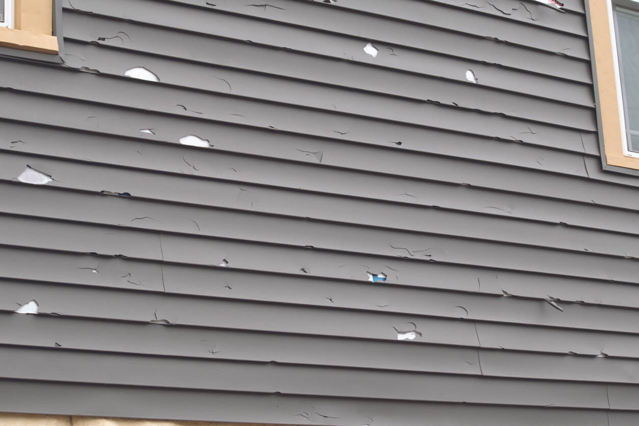 Gray vinyl siding with extensive storm damage, including cracks, holes, and missing sections. Severe weather can cause significant exterior damage, leading to energy loss and structural issues. Empire Contractors specializes in storm damage repair and siding replacement to restore and protect homes.